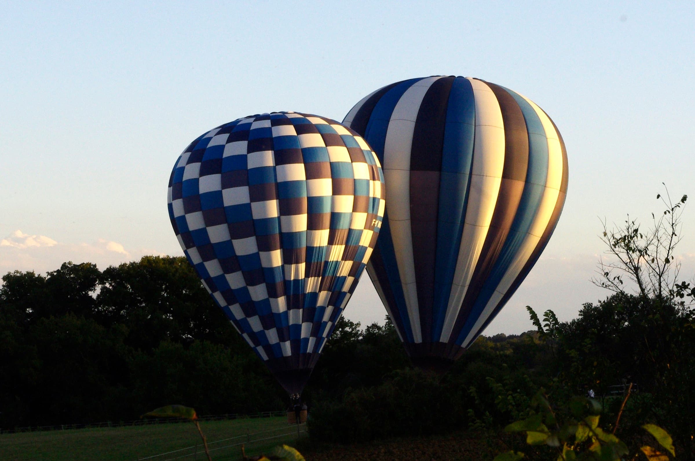 Two hot air balloons landing in a grass field at dusk near Saint Clar