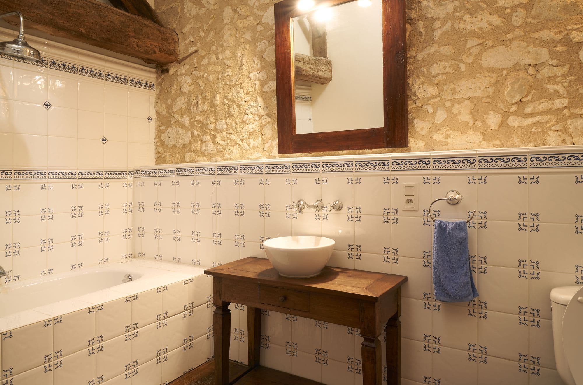A bathroom with a bath, a vessel basin on an antique wooden table and patterned tiling