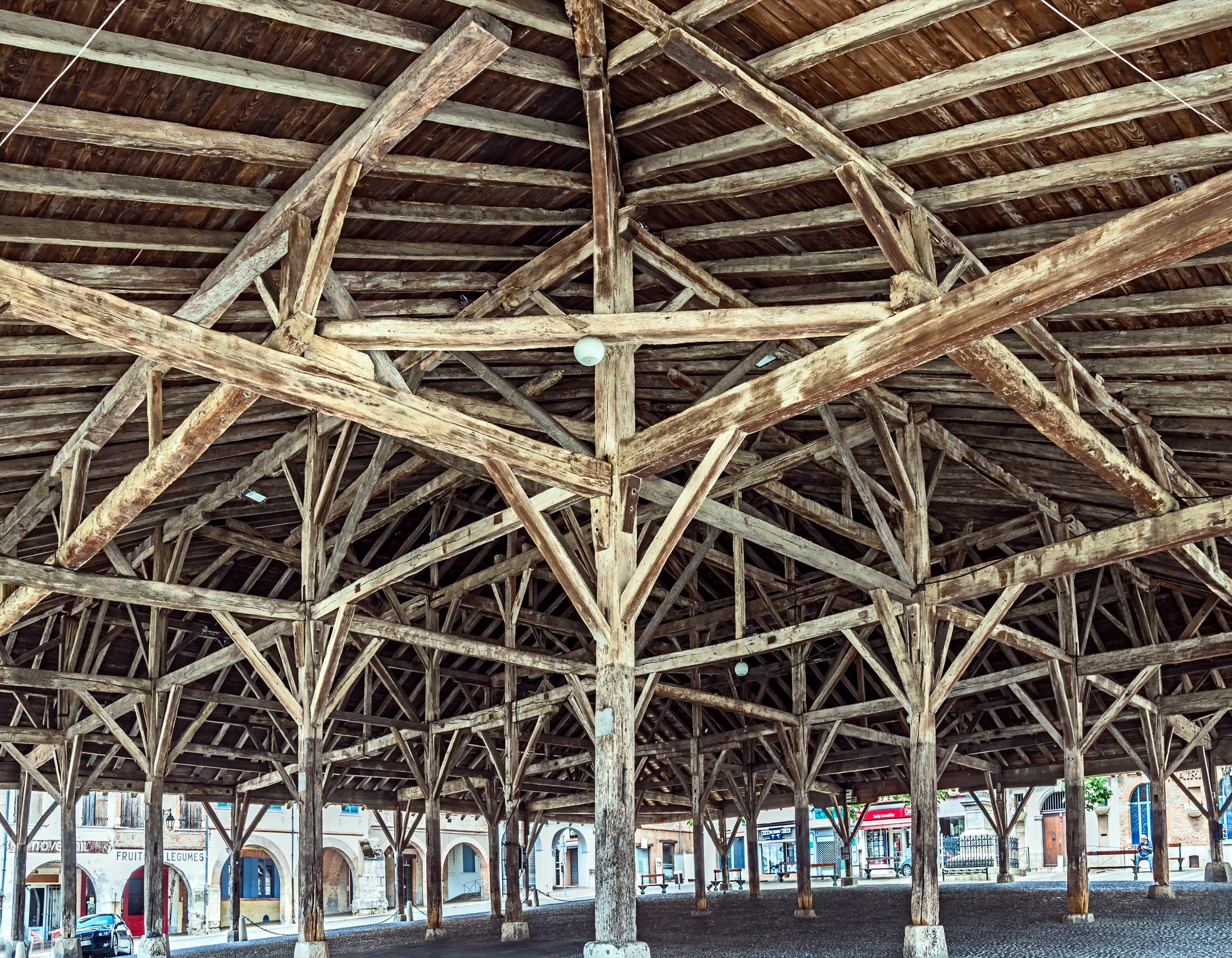 Looking up into the medieval oak roof of the market hall at Beaumont-de-Lomagne, a web of beams on tall timber posts