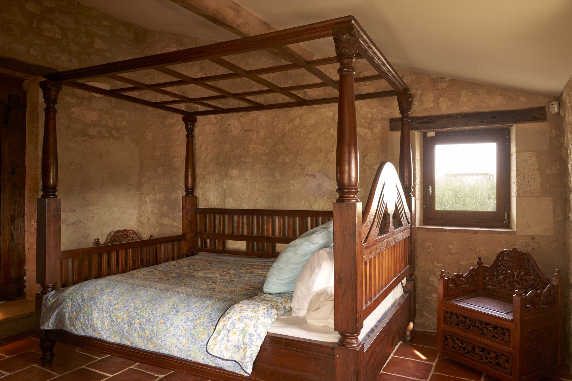 A bedroom with a carved wooden four-poster king bed on a terracotta floor