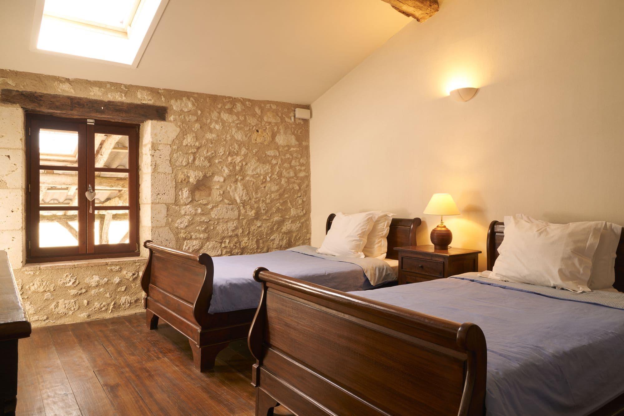 A bedroom with two twin sleigh beds, a stone wall and an oak lintel