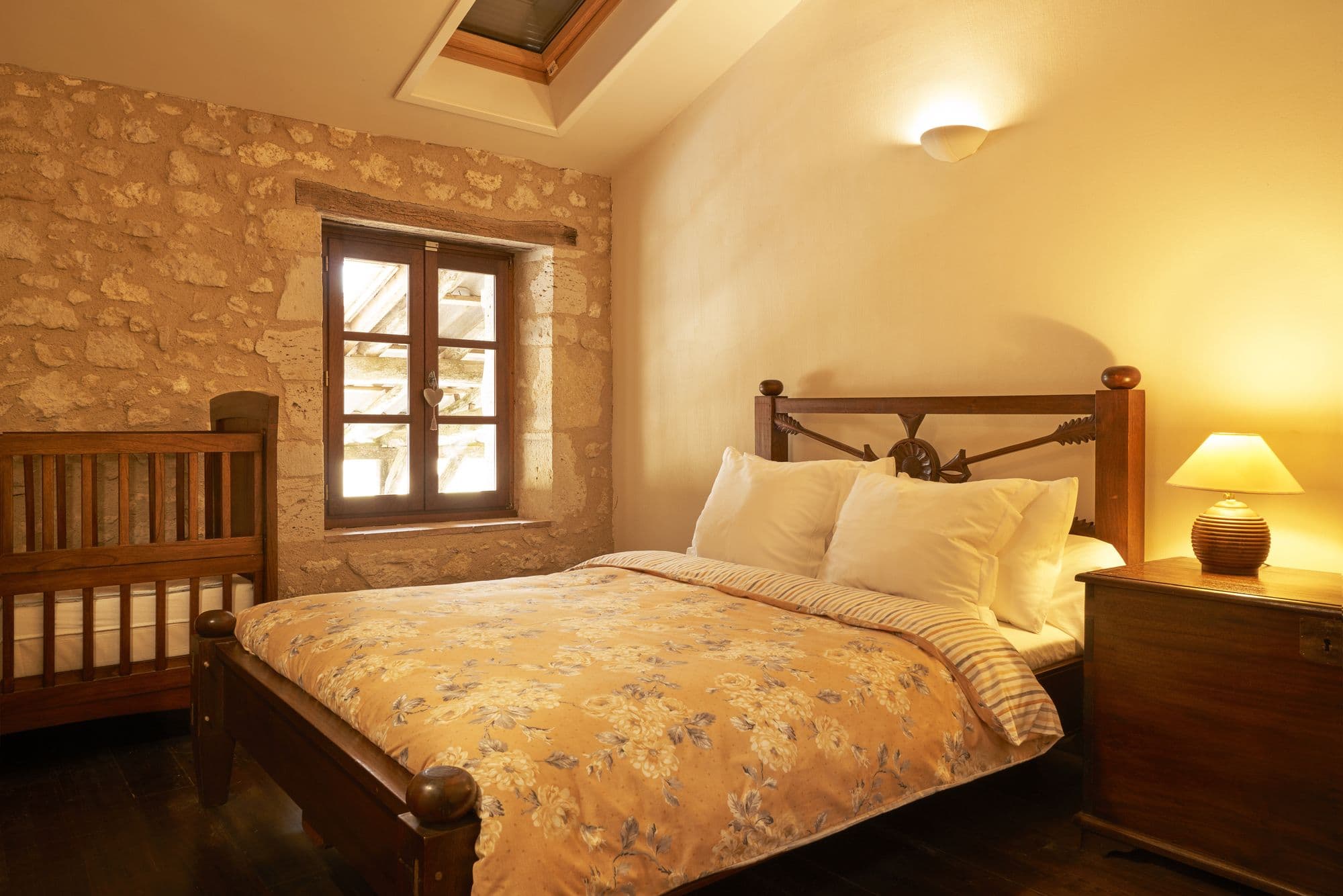 A bedroom with a king bed, a stone wall and a skylight