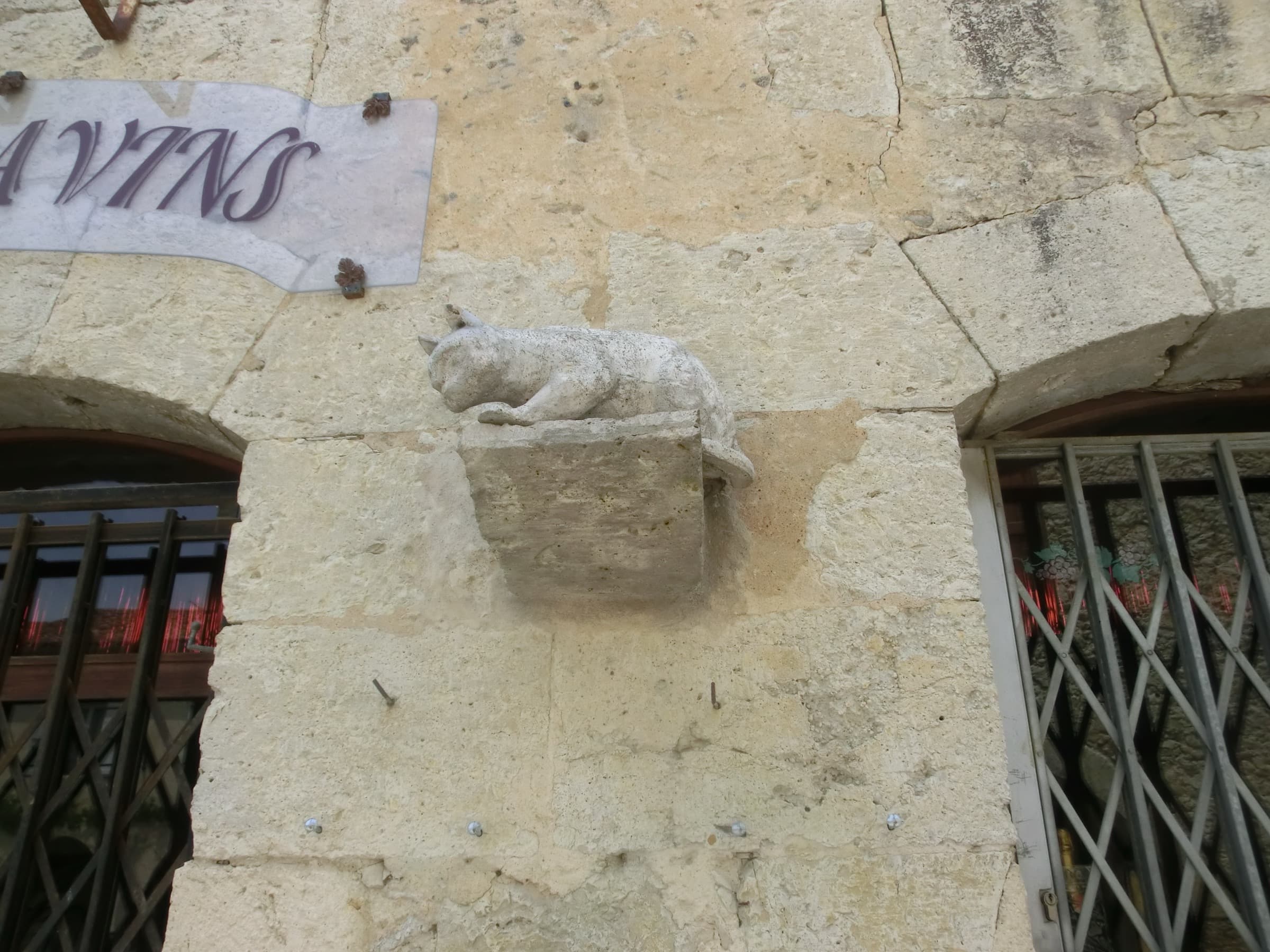 A carved stone cat stretched out on a corbel on a limestone house wall at La Romieu