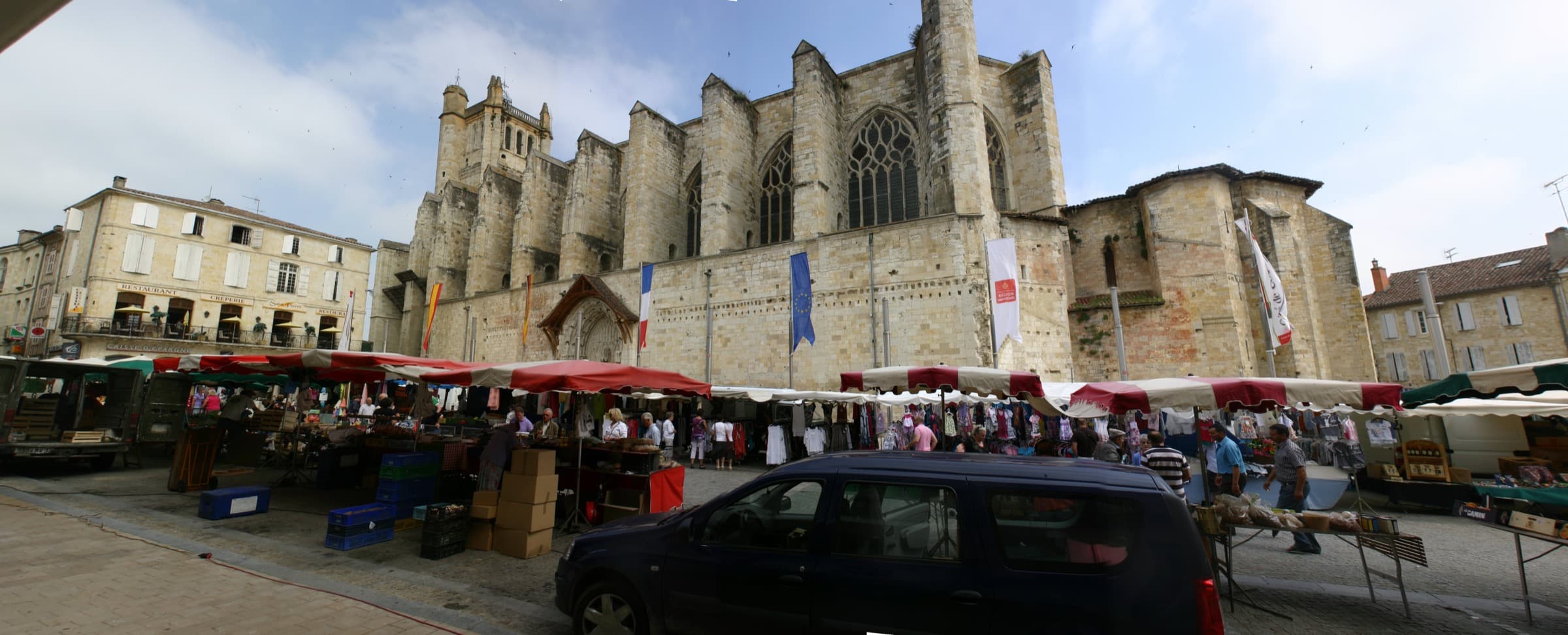 Market stalls with red and white awnings set out along the front of the Gothic cathedral at Condom
