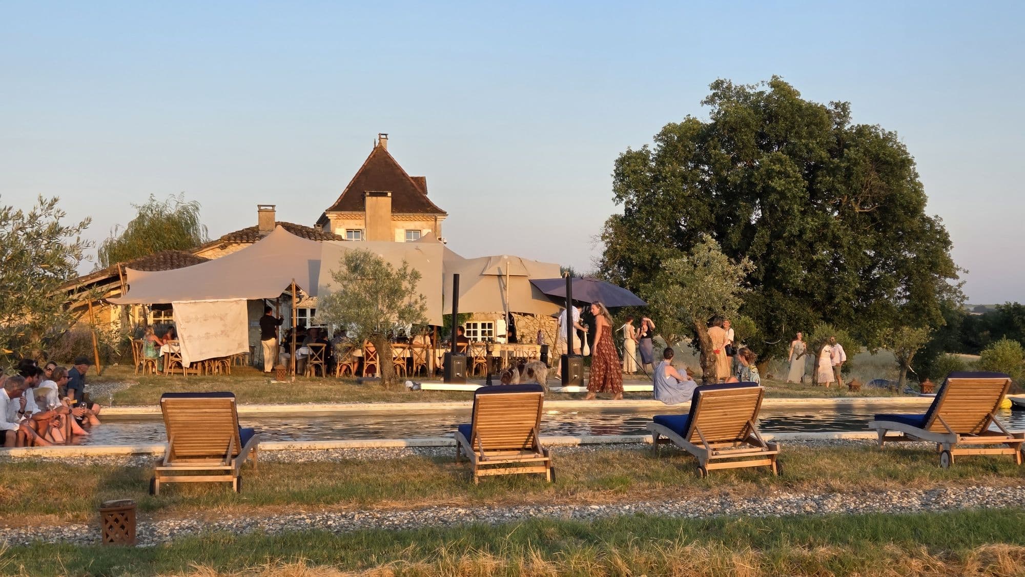 The house at golden hour with a stretch marquee beside the pool and guests on the lawn